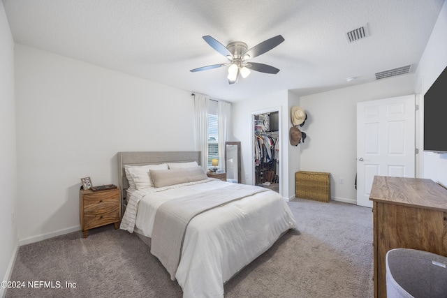 bedroom with ceiling fan, a spacious closet, a textured ceiling, light colored carpet, and a closet