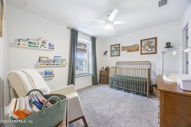 carpeted bedroom with ceiling fan and a crib