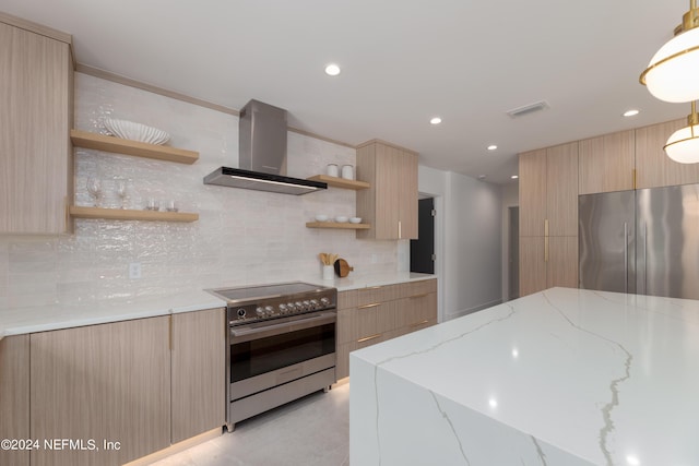 kitchen featuring wall chimney range hood, appliances with stainless steel finishes, tasteful backsplash, decorative light fixtures, and light stone counters