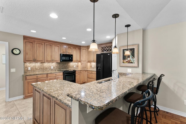 kitchen featuring kitchen peninsula, light stone countertops, sink, black appliances, and hanging light fixtures