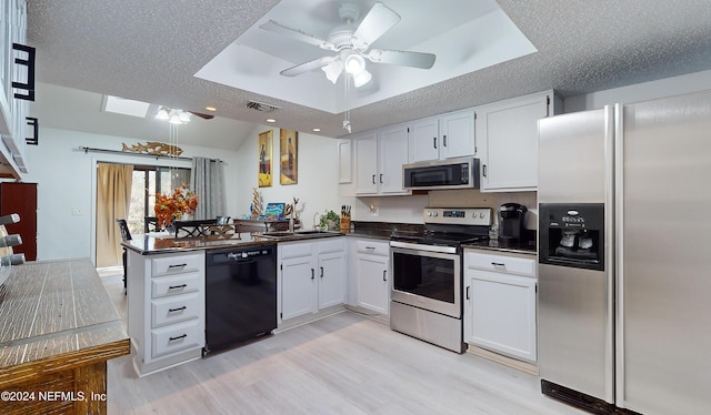 kitchen featuring white cabinets, a skylight, ceiling fan, kitchen peninsula, and stainless steel appliances