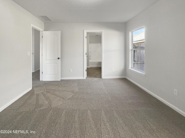 unfurnished bedroom featuring dark colored carpet, a textured ceiling, a spacious closet, and a closet