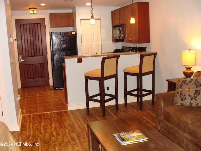 kitchen with kitchen peninsula, a kitchen breakfast bar, black appliances, hardwood / wood-style flooring, and hanging light fixtures