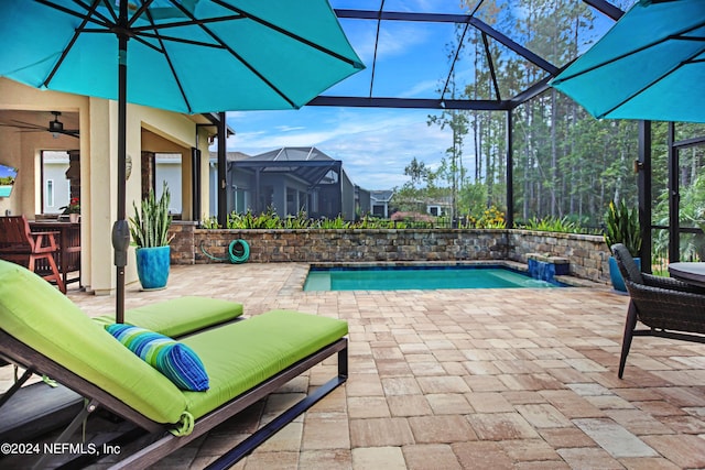 view of swimming pool with glass enclosure, ceiling fan, and a patio area