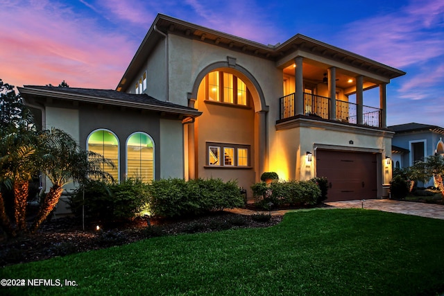 view of front of house with a balcony, a garage, ceiling fan, and a lawn