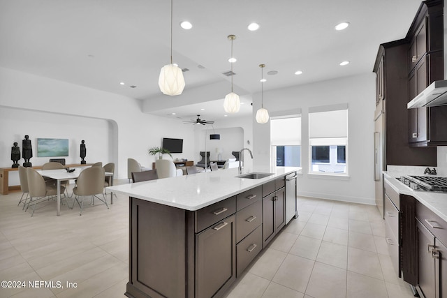 kitchen with ceiling fan, sink, wall chimney range hood, decorative light fixtures, and a kitchen island with sink