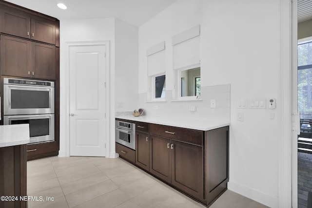 kitchen featuring dark brown cabinets, decorative backsplash, light tile patterned floors, and double oven