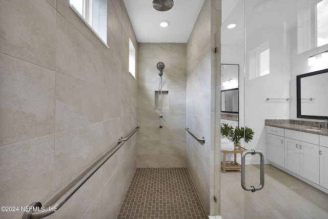 bathroom with tile patterned flooring, a tile shower, and vanity