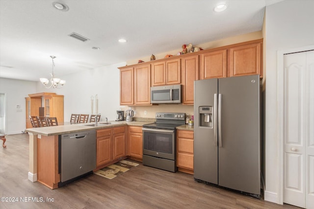 kitchen featuring an inviting chandelier, wood-type flooring, hanging light fixtures, kitchen peninsula, and stainless steel appliances