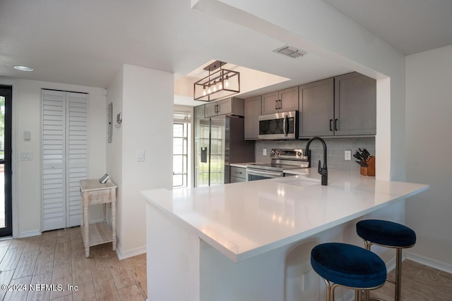 kitchen featuring kitchen peninsula, backsplash, a breakfast bar, stainless steel appliances, and sink