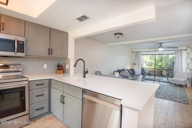 kitchen with backsplash, kitchen peninsula, sink, and appliances with stainless steel finishes