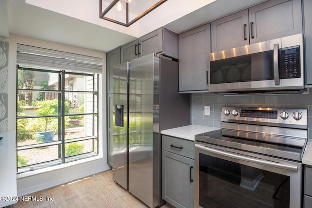 kitchen featuring backsplash, gray cabinets, light hardwood / wood-style flooring, and stainless steel appliances