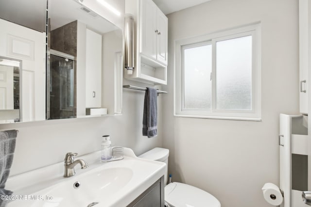 bathroom featuring a shower with door, vanity, a healthy amount of sunlight, and toilet