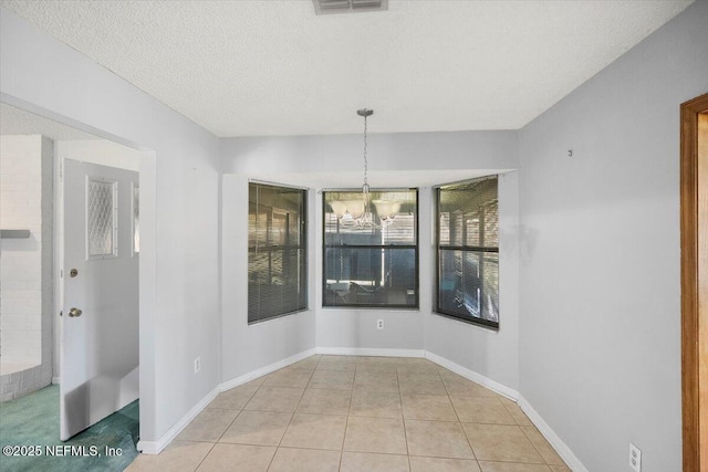 unfurnished dining area with a notable chandelier, light tile patterned floors, and a textured ceiling