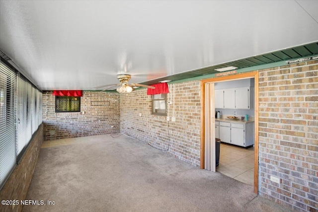 unfurnished living room with light colored carpet, ceiling fan, and brick wall