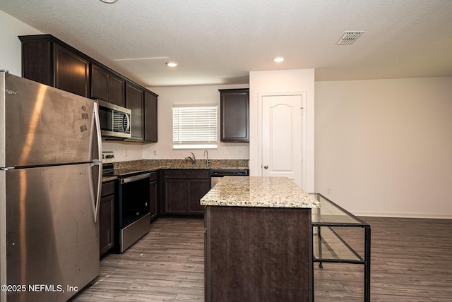 kitchen with light stone countertops, dark brown cabinetry, stainless steel appliances, hardwood / wood-style flooring, and a center island