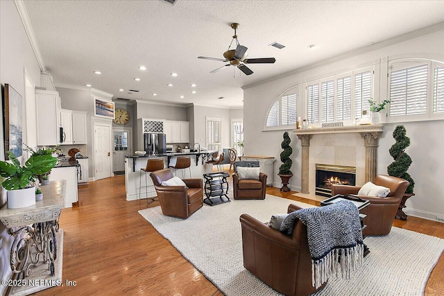 living room featuring a textured ceiling, light hardwood / wood-style flooring, ornamental molding, and a tiled fireplace