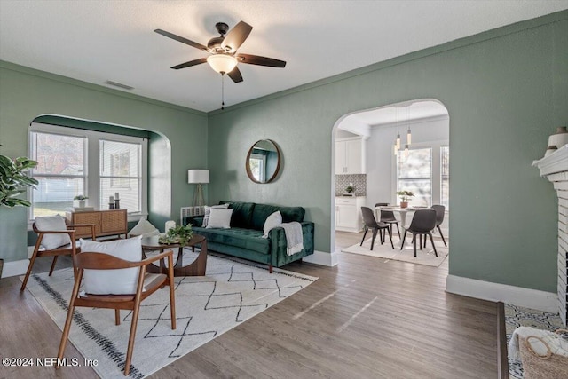 living room featuring ceiling fan, ornamental molding, and light wood-type flooring