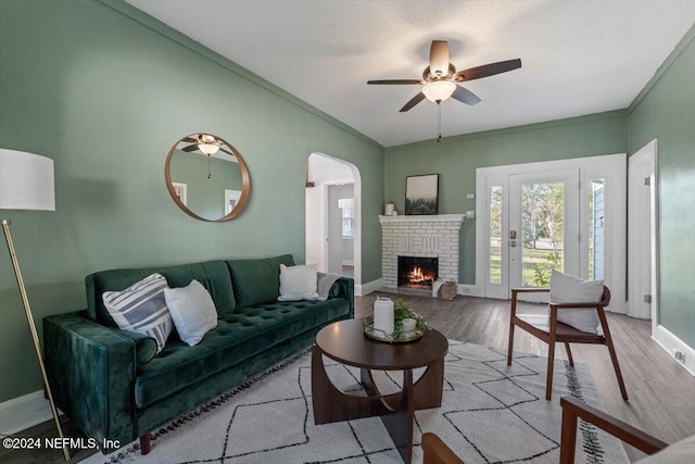 living room featuring a textured ceiling, ceiling fan, crown molding, a fireplace, and light hardwood / wood-style floors