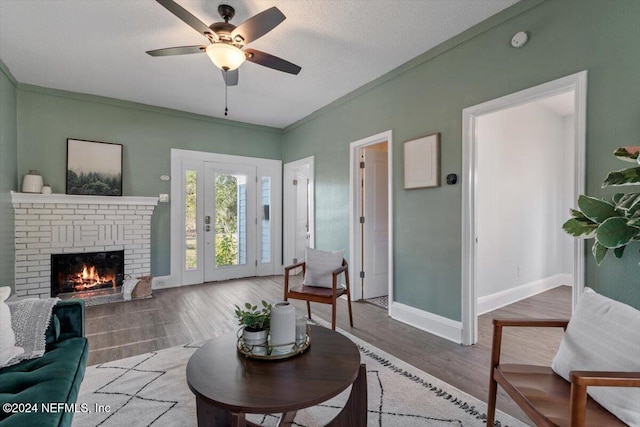 living room with hardwood / wood-style floors, a brick fireplace, ceiling fan, ornamental molding, and a textured ceiling