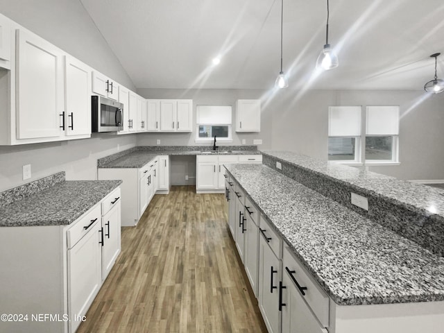 kitchen with white cabinetry, sink, hardwood / wood-style floors, dark stone counters, and decorative light fixtures