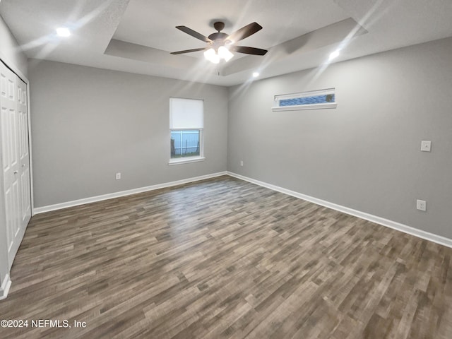 unfurnished bedroom featuring a closet, a raised ceiling, ceiling fan, and dark hardwood / wood-style floors