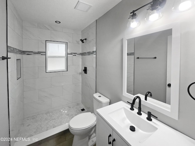 bathroom with a tile shower, tile patterned flooring, vanity, and toilet