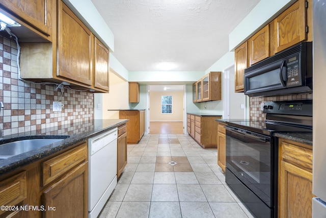 kitchen with dark stone counters, light tile patterned floors, decorative backsplash, brown cabinetry, and black appliances