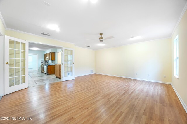 unfurnished living room with french doors, ornamental molding, ceiling fan, a healthy amount of sunlight, and light hardwood / wood-style flooring