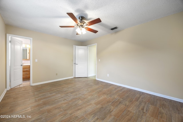 unfurnished bedroom featuring ensuite bath, ceiling fan, wood-type flooring, and a textured ceiling