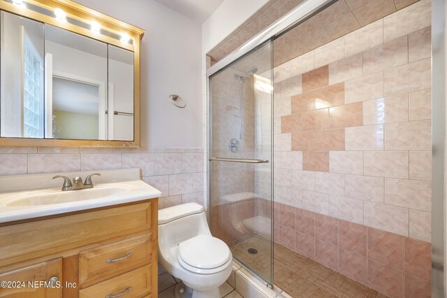 bathroom featuring walk in shower, tasteful backsplash, toilet, vanity, and tile walls