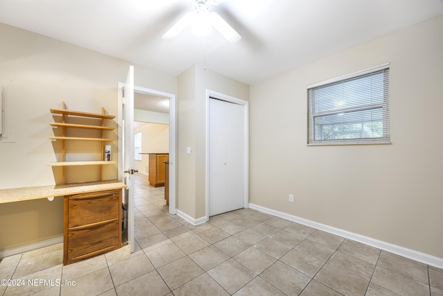 unfurnished bedroom with light tile patterned floors, built in desk, a closet, and ceiling fan