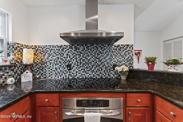 kitchen featuring decorative backsplash, oven, dark stone counters, and wall chimney range hood