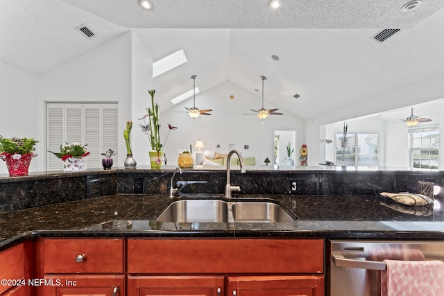 kitchen with dishwasher, dark stone countertops, lofted ceiling with skylight, and sink