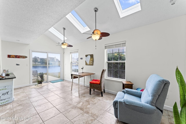 living area featuring ceiling fan, lofted ceiling with skylight, a textured ceiling, a water view, and light tile patterned floors