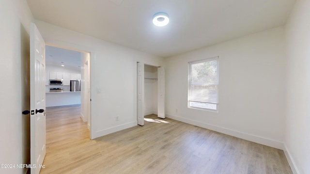 unfurnished bedroom with a closet, stainless steel fridge, and light hardwood / wood-style flooring