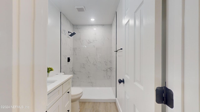 bathroom with hardwood / wood-style flooring, tiled shower, vanity, and toilet