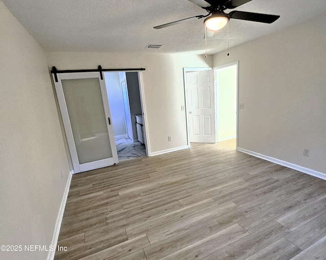 empty room featuring light wood-type flooring, a textured ceiling, a barn door, and ceiling fan