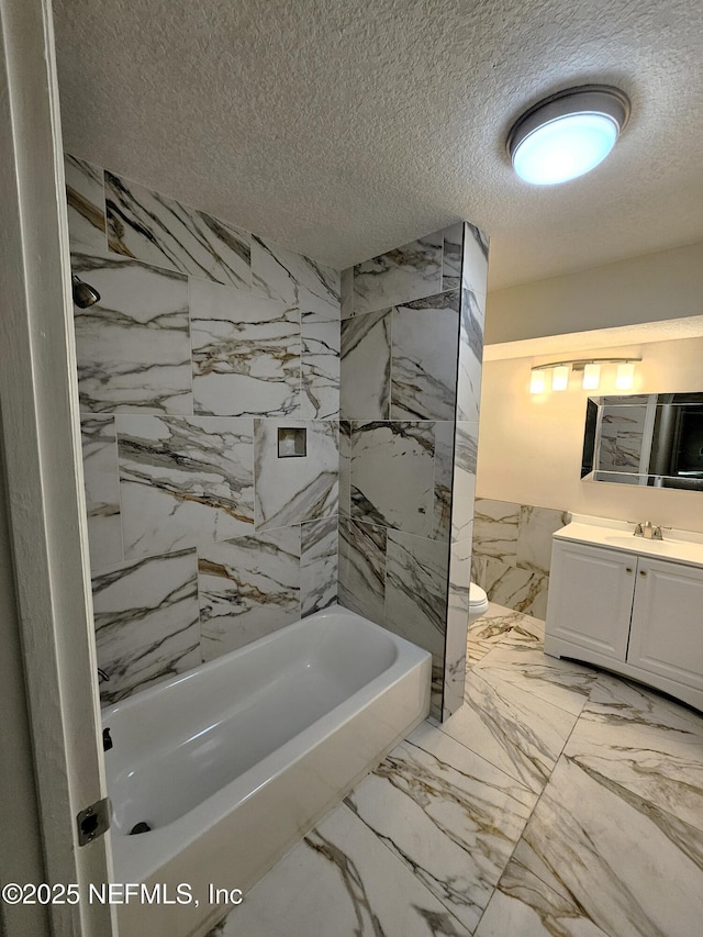 full bathroom with vanity, tiled shower / bath combo, a textured ceiling, and toilet