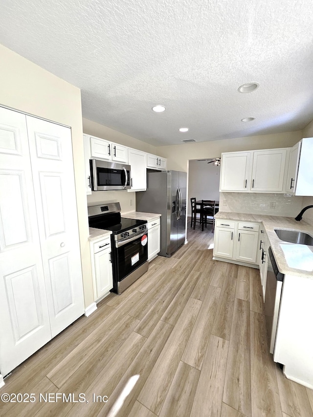 kitchen featuring sink, light hardwood / wood-style flooring, a textured ceiling, white cabinets, and appliances with stainless steel finishes