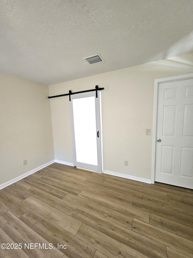 empty room featuring hardwood / wood-style floors, a barn door, and a textured ceiling