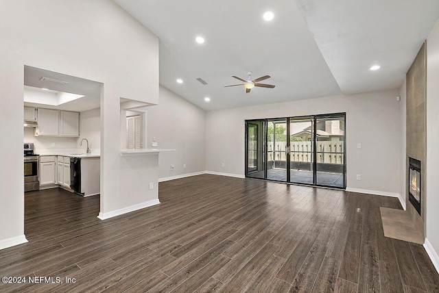 unfurnished living room with dark wood-type flooring, a large fireplace, ceiling fan, and vaulted ceiling