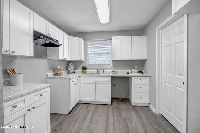 kitchen featuring white cabinets, light hardwood / wood-style floors, light stone counters, and sink