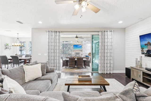 living room featuring ceiling fan with notable chandelier, hardwood / wood-style floors, a textured ceiling, and wooden walls