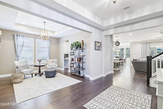 sitting room with dark hardwood / wood-style flooring, a raised ceiling, and a chandelier