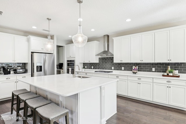 kitchen featuring white cabinetry, hanging light fixtures, appliances with stainless steel finishes, and wall chimney exhaust hood