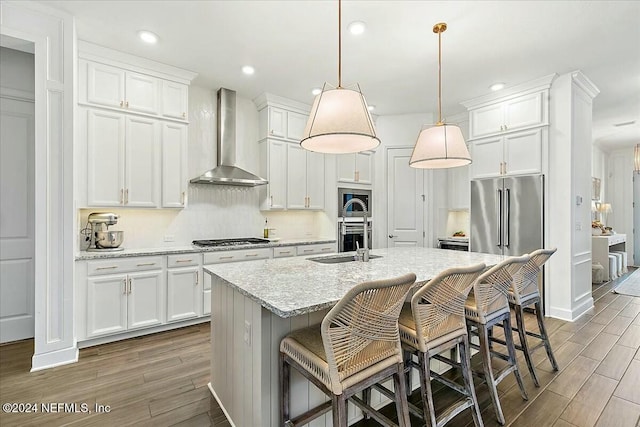 kitchen featuring white cabinets, hanging light fixtures, wall chimney exhaust hood, and a center island with sink