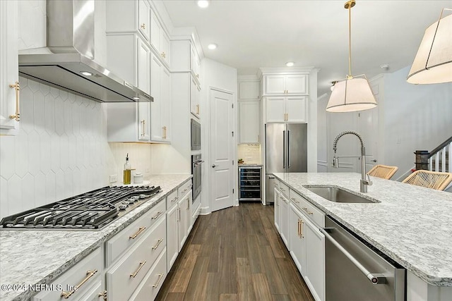 kitchen featuring wall chimney range hood, sink, appliances with stainless steel finishes, tasteful backsplash, and decorative light fixtures