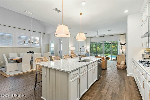 kitchen featuring decorative light fixtures, an island with sink, sink, a kitchen breakfast bar, and light stone countertops