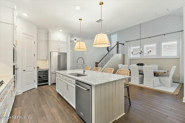 kitchen with stainless steel appliances, an island with sink, hanging light fixtures, and wine cooler